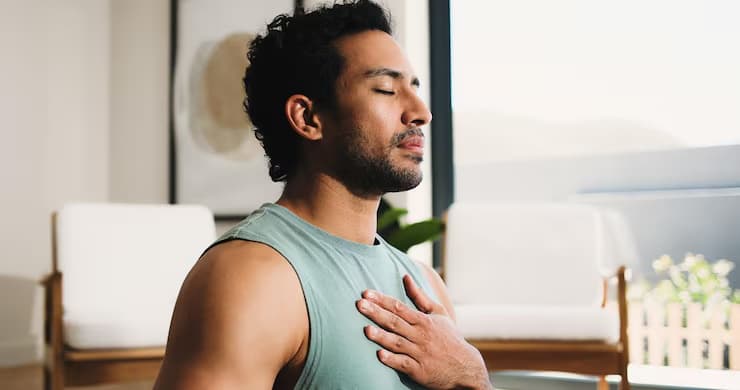 A person sitting with eyes closed, one hand resting on their chest, breathing